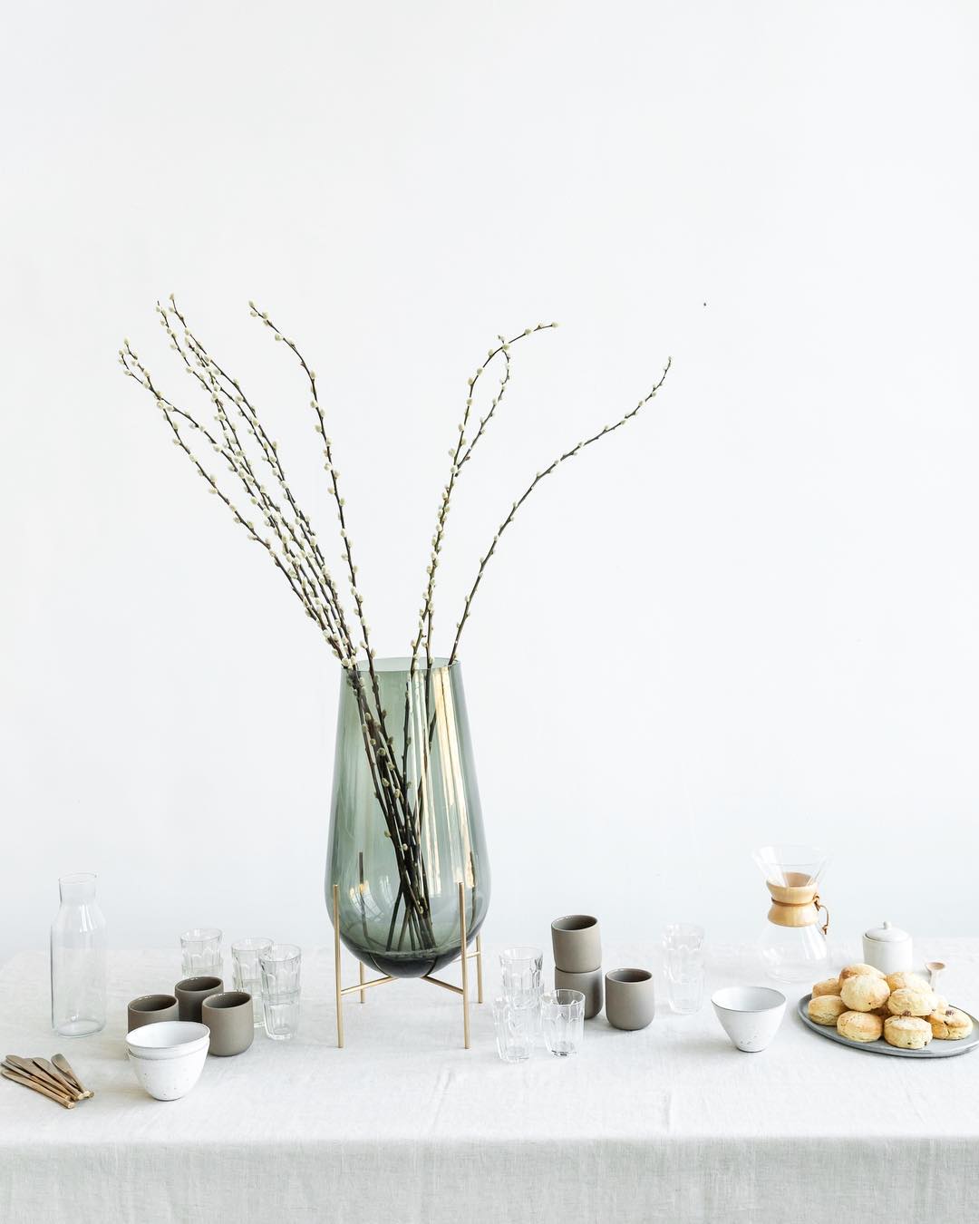 White table setting with a big green vase, ceramic coffee cups and scones